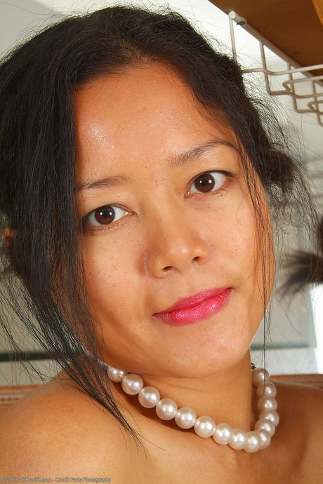 Den asiatiske kvinde Adena går nøgen i sit køkken iført høje hæle