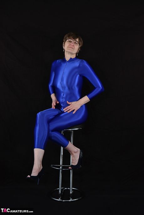 Moden tysk dame i en latex bodysuit, der afslører sine små bryster og skaldede fisse