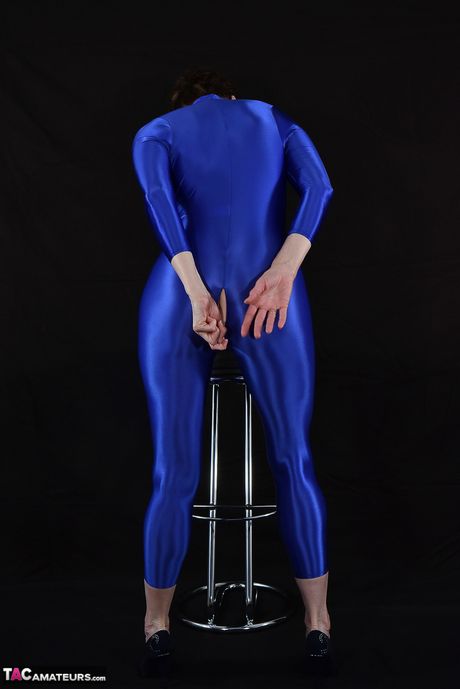 Moden tysk dame i en latex bodysuit, der afslører sine små bryster og skaldede fisse