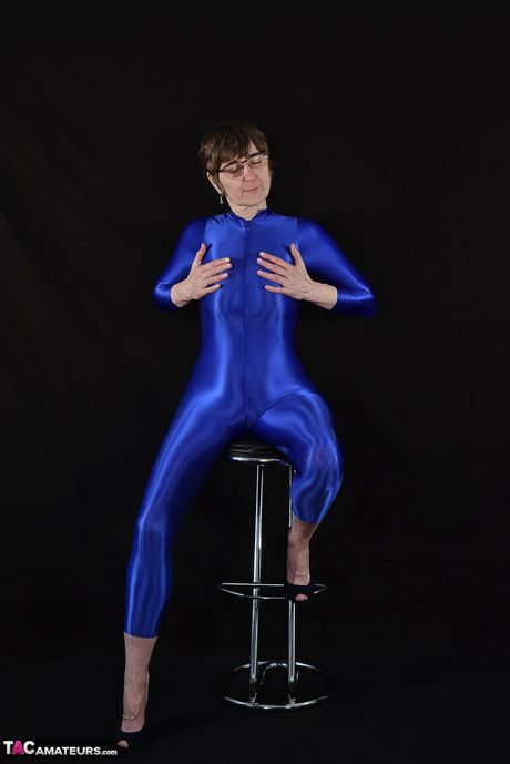 Moden tysk dame i en latex bodysuit, der afslører sine små bryster og skaldede fisse