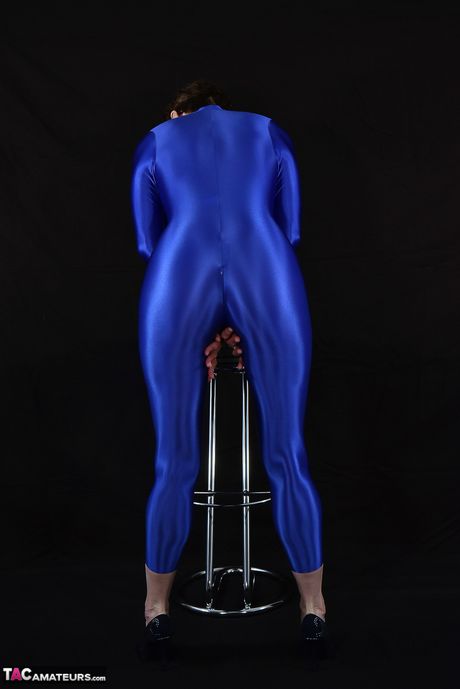 Moden tysk dame i en latex bodysuit, der afslører sine små bryster og skaldede fisse