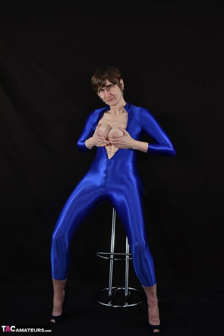 Moden tysk dame i en latex bodysuit, der afslører sine små bryster og skaldede fisse