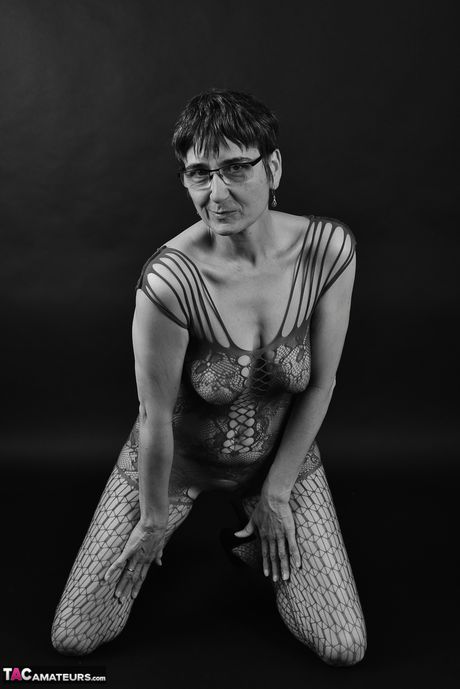 穿著緊身連身衣和眼鏡的成年德國女士脫掉衣服到她的絲襪