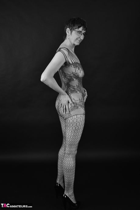 穿著緊身連身衣和眼鏡的成年德國女士脫掉衣服到她的絲襪